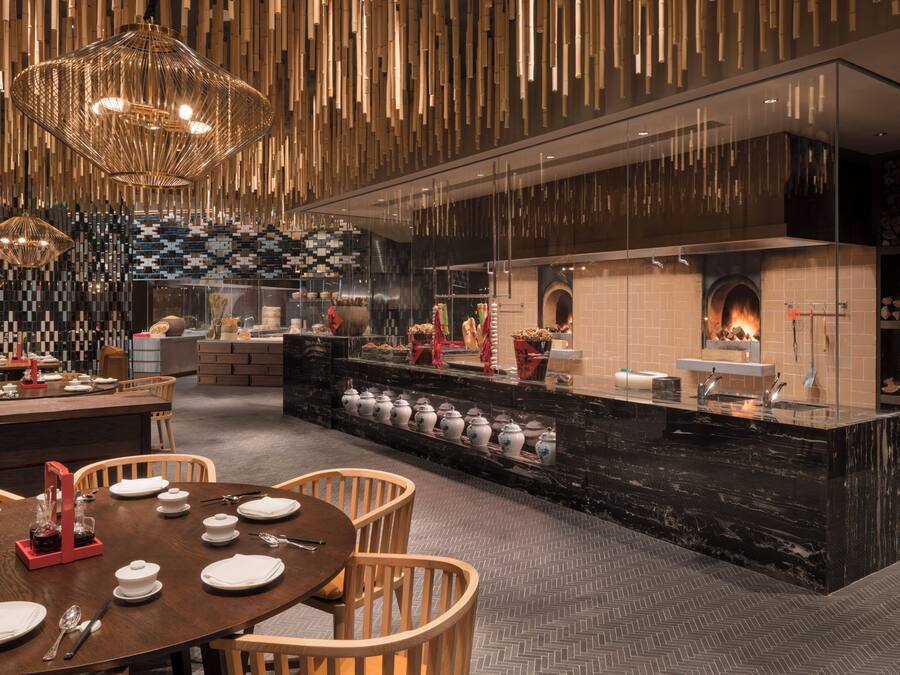 A modern restaurant with a central island, wooden chairs, and hanging light fixtures.