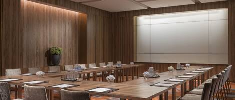 Un salón de conferencias con una larga mesa de madera, varias sillas y una pizarra grande.