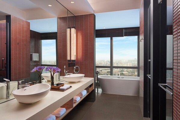 A modern bathroom with a large window, a bathtub, and two sinks.