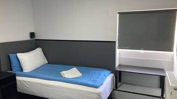 Una habitación de hotel con cama, mesita de noche, escritorio y silla, y ventana.