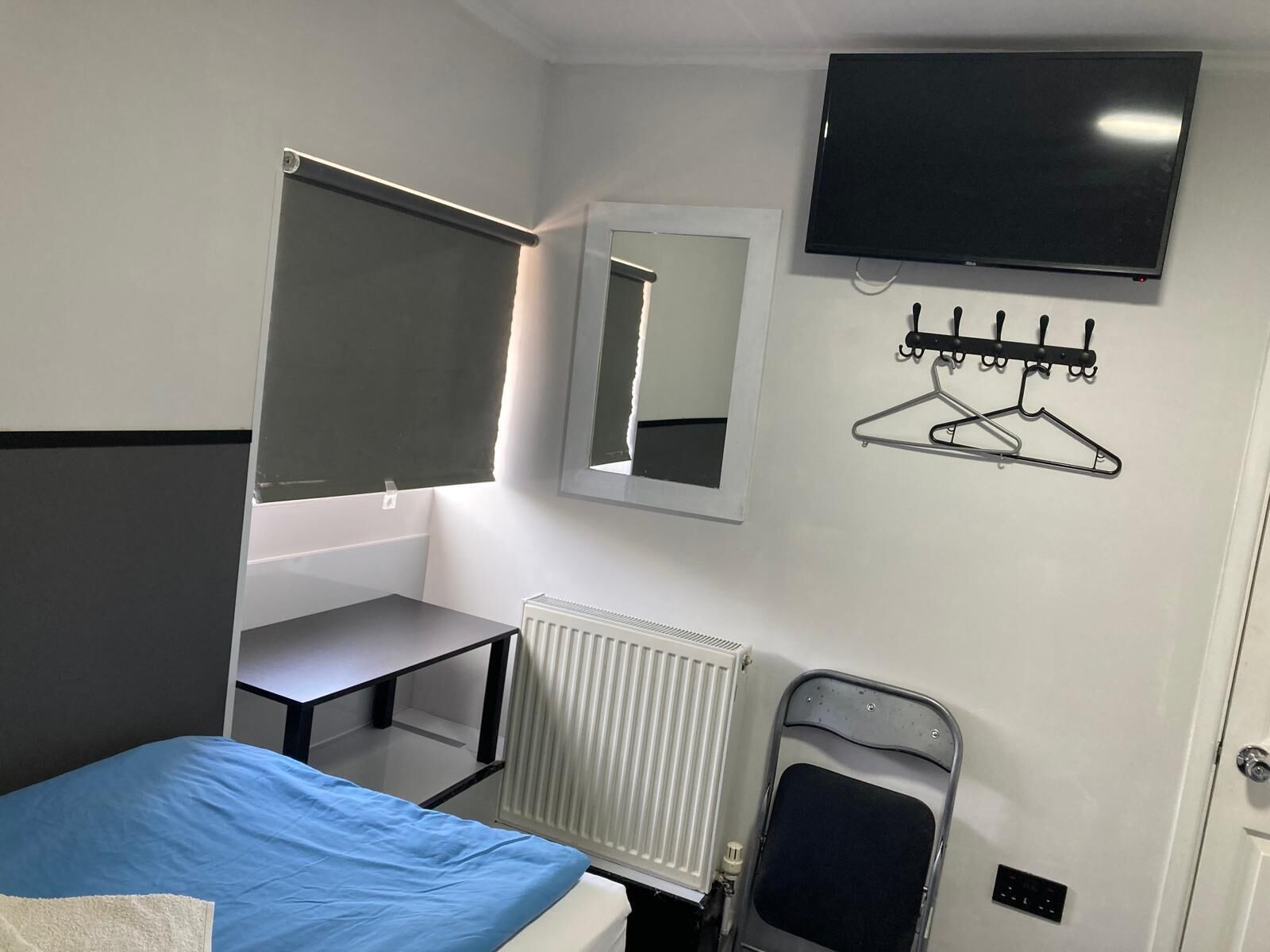 Een hotelkamer met een bed, bureau, spiegel, televisie, radiator en kapstok.