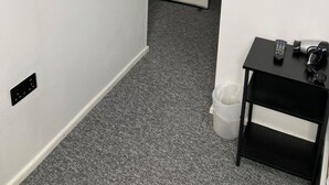 Un pasillo con una puerta blanca marcada con el número 7, una pequeña mesa negra con un control remoto y un mapa enmarcado en la pared.