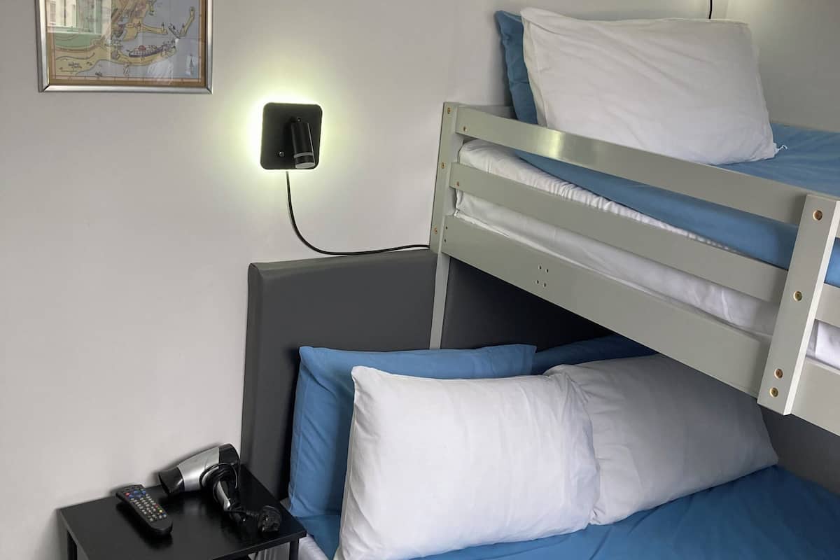 A single bed with blue bedding, a bedside table with a remote control, a map on the wall, and a wall-mounted light.