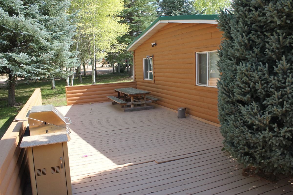 A wooden cabin with a deck, picnic table, and barbecue grill.