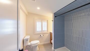 A bathroom with a toilet, a window, and a shower area.