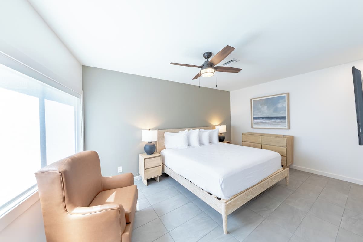 A bedroom with a bed, nightstands, a chair, a ceiling fan, and a painting on the wall.