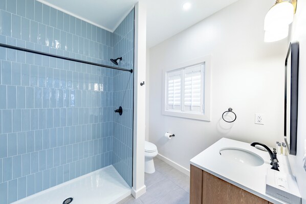 A bathroom with a shower, toilet, sink, and mirror. - The Palmetto Inn (Boca Grande)