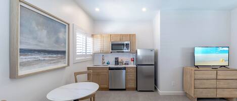 A compact kitchen with a microwave, refrigerator, and dishwasher, a dining area with a table and chairs, and a TV on a wooden cabinet.