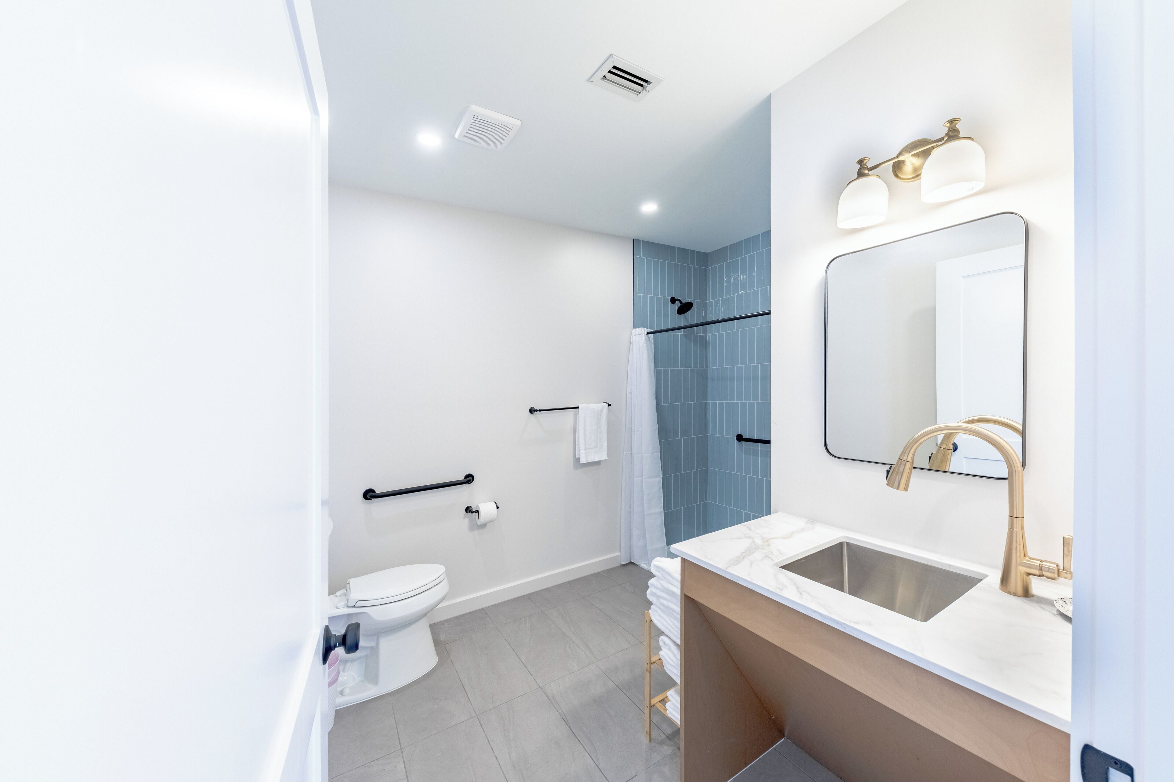 Een moderne badkamer met een wit toilet, een wastafel met gouden kraan, een spiegel en een douchehoek.