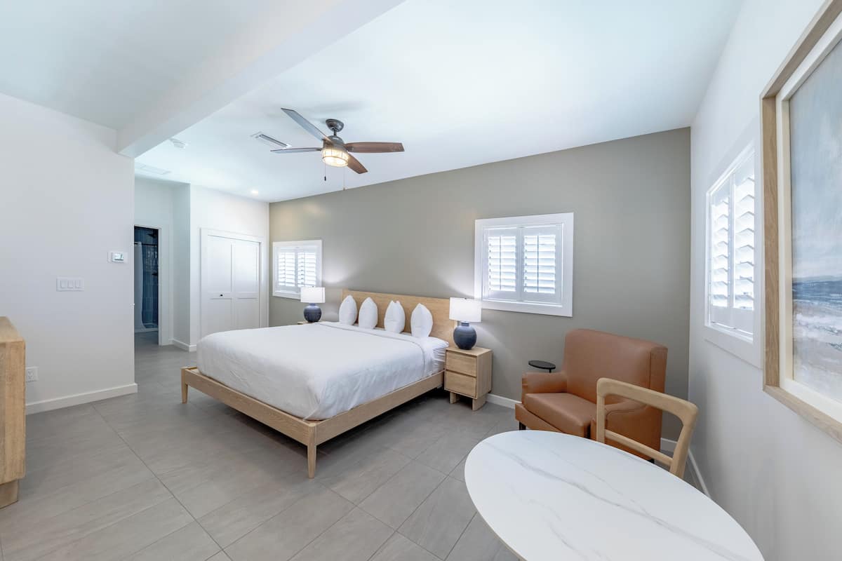A bedroom with a bed, bedside tables, a chair, a ceiling fan, and a window.