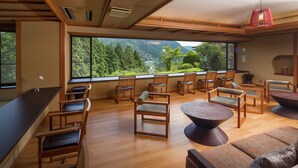 A modern interior with wooden furniture, a large window offering a view of greenery and mountains, and a bar area. - Washintei Hogetsu (Hakone)
