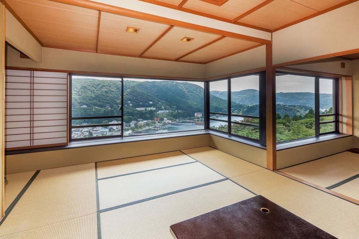 A tatami mat room with large windows offering a view of a mountainous landscape.