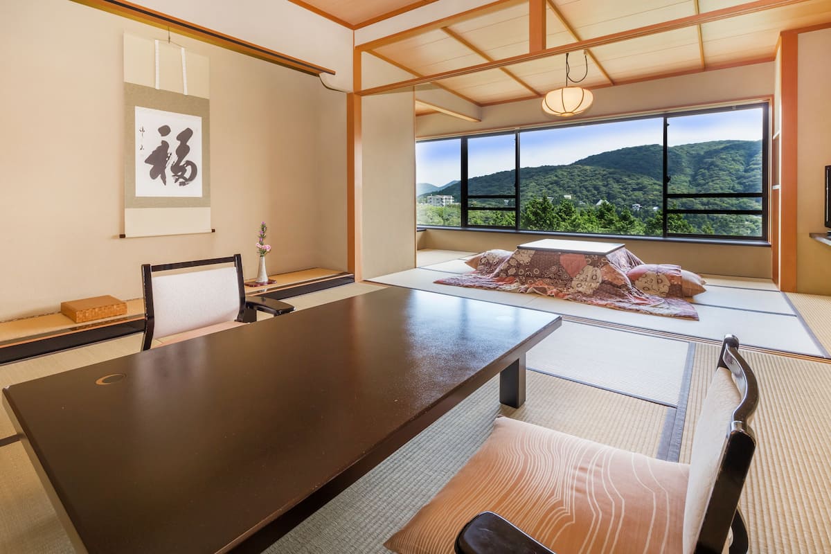 A traditional Japanese room with tatami flooring, a low table, and a view of a mountainous landscape through large windows.