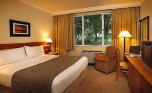 Une chambre d’hôtel avec un lit, une chaise, un bureau avec un ordinateur et une fenêtre avec des rideaux.