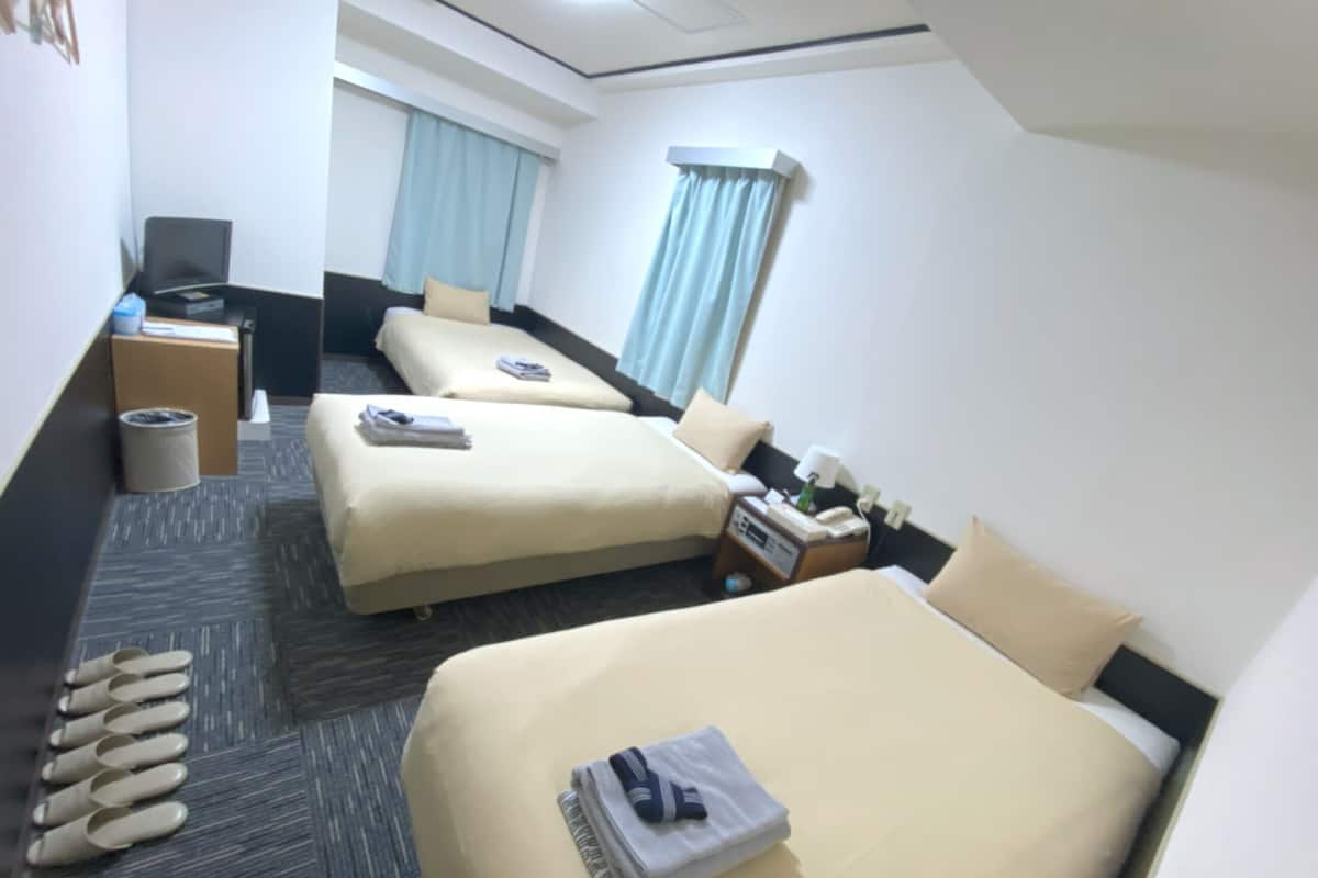 A hotel room with two beds, a desk, a chair, a trash bin, and a window with curtains.