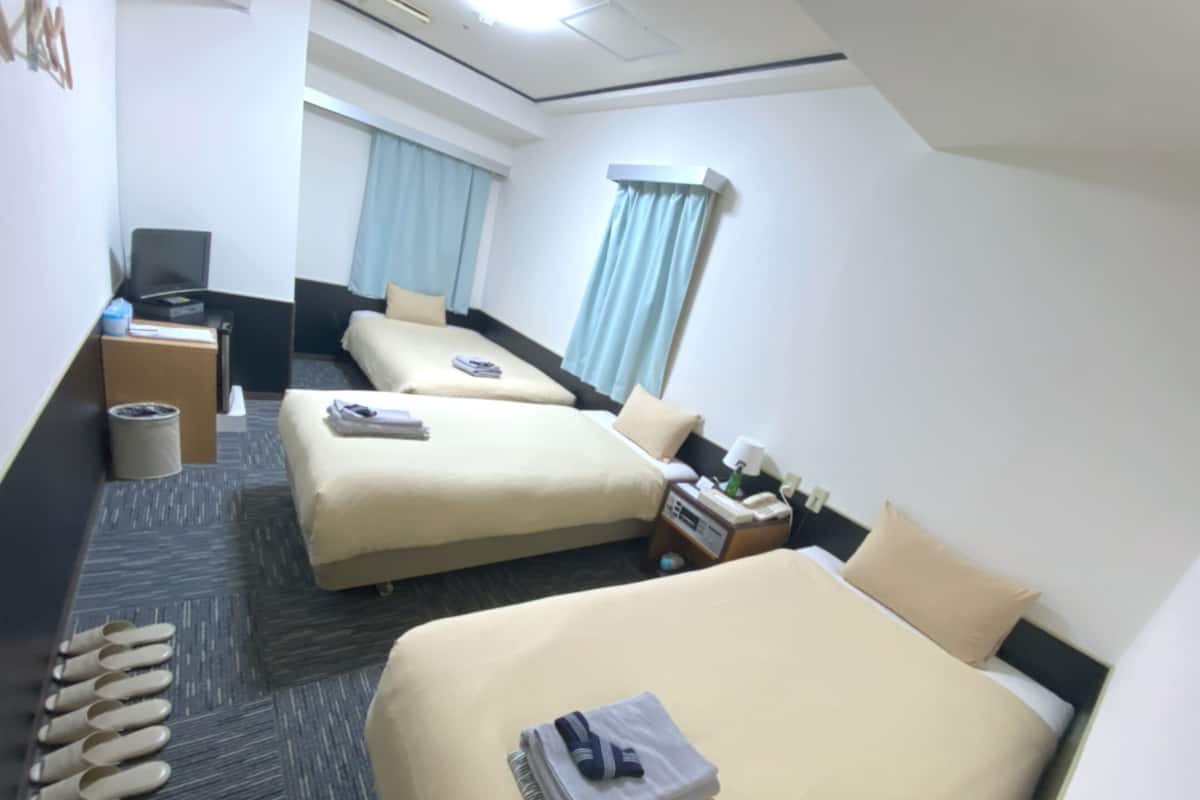 A hotel room with two beds, a desk, a chair, a trash bin, and a window with curtains.