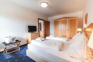 A hotel room with a bed, a desk, a television, wooden wardrobes, and a lamp.