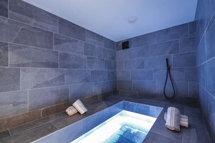 Un baño moderno con baldosas de piedra oscura, una bañera empotrada y zona de ducha.