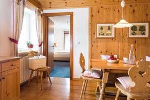 A wooden-floored room with a bed, a dining table with chairs, a basket, and a wall-mounted lamp. - Monte Croce Hotel Kreuzberg (Sesto)