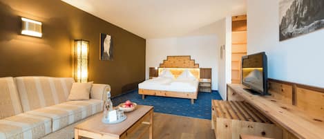 Ein modernes Hotelzimmer mit einem hölzernen Bett, einer Couch, einem Fernseher und einem Esstisch.