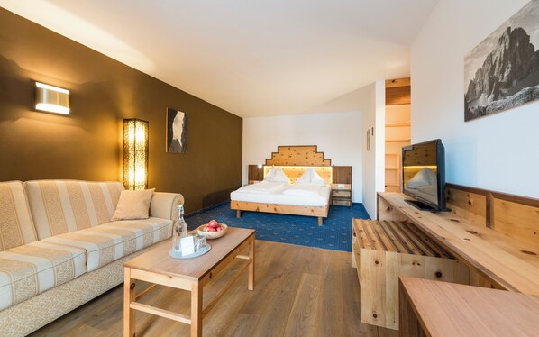 A modern hotel room with a wooden bed, a sofa, a TV, and a dining table.