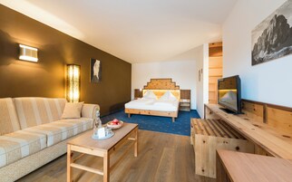Una habitación de hotel moderna con una cama de madera, un sofá, un televisor y una mesa de comedor.