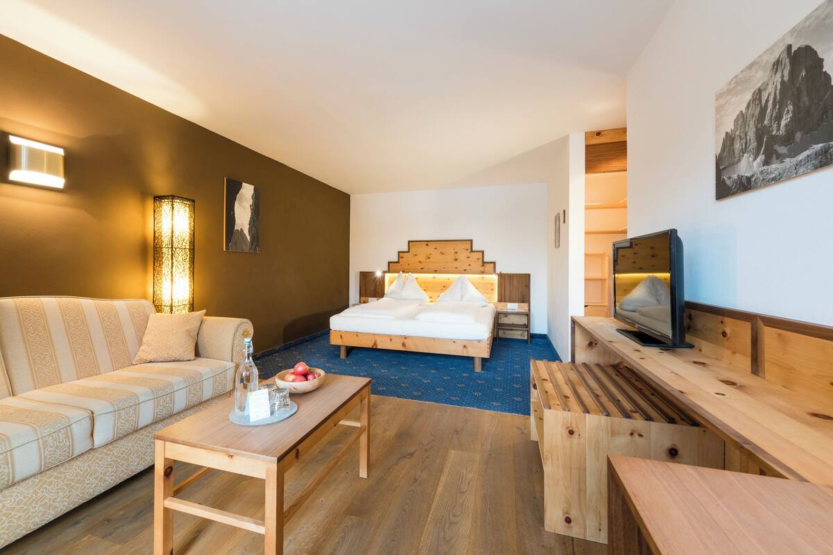 Una habitación de hotel moderna con una cama de madera, un sofá, un televisor y una mesa de comedor.