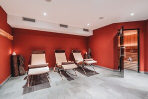 A spa room with three reclining chairs, a wooden shelf with towels, and a wooden door leading to another room. - Monte Croce Hotel Kreuzberg (Sesto)