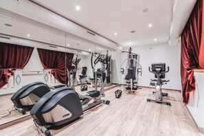 Une salle de sport équipée de divers appareils d’exercice, dotée d’un grand miroir et d’un sol en bois.