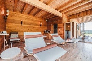 A wooden cabin interior with four reclining chairs, a small table, and a glass door leading outside.