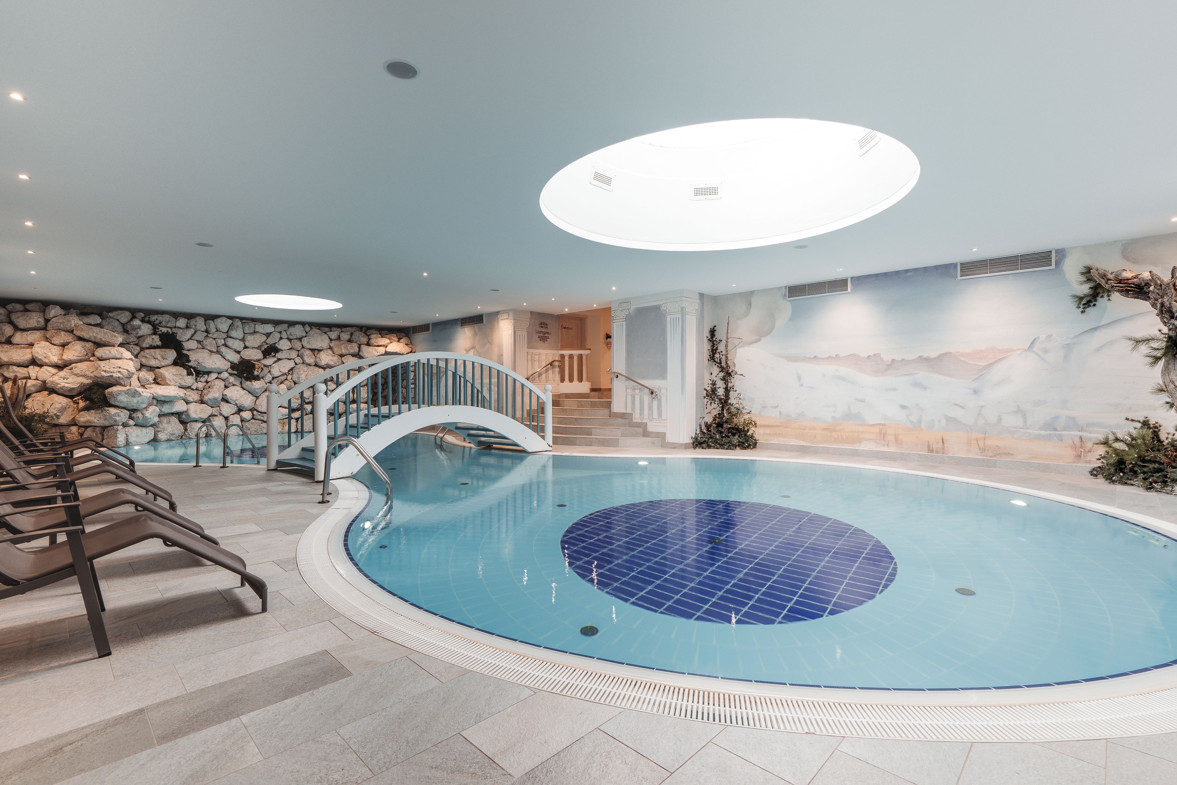 Una piscina interior con un fondo de pared de piedra, una escalera y una lámpara en el techo.