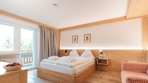 Un dormitorio con una cama de madera, una mesita de noche, una silla con estampado de cuadros rojos y una ventana con cortinas.