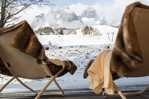 Twee stoelen met bont bekleding kijken uit op een besneeuwd berglandschap met een skilift op de achtergrond.