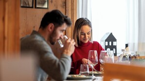Un tavolo da pranzo con bicchieri da vino e piatti, in una stanza con pareti in legno e una casa in miniatura sul tavolo.