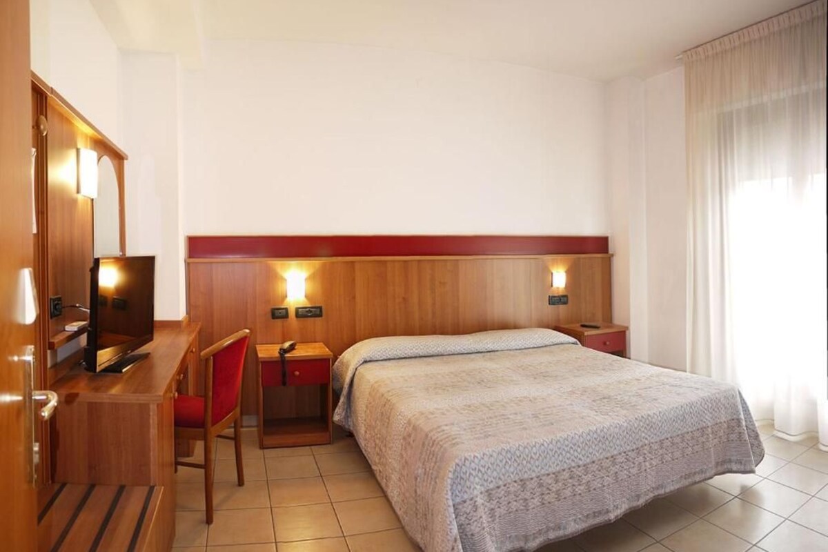 Una habitación de hotel con una cama, un escritorio con una silla, un televisor y un espejo.