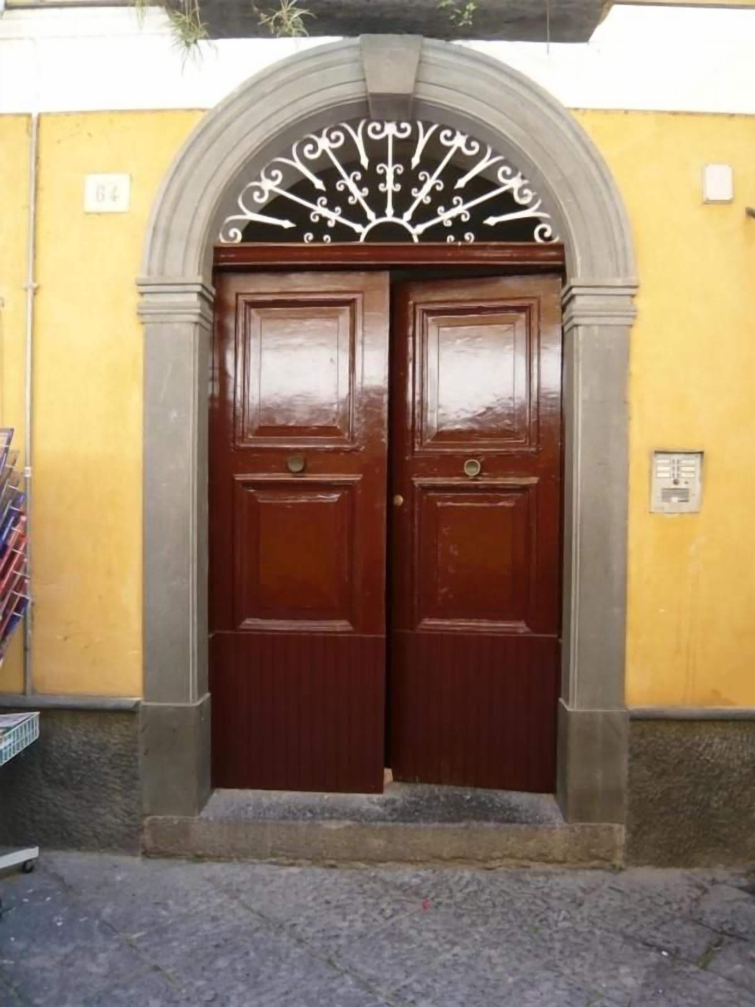 A double wooden door with a decorative metal arch above it, set in a yellow wall with a stone base.