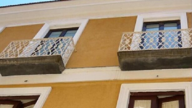 A building with a yellow facade, two balconies with lattice railings, and a window with a wooden frame. - DolceVita Sorrento Guest House (Sorrento)