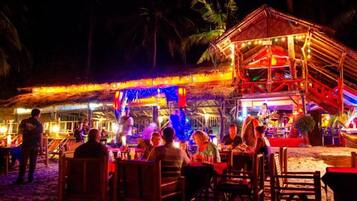 An outdoor dining area with tables and chairs, a stage with performers, and a covered seating area.