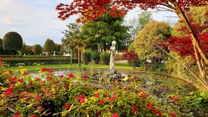 Un jardin agrémenté d’une statue, d’un bassin et de différents arbres.