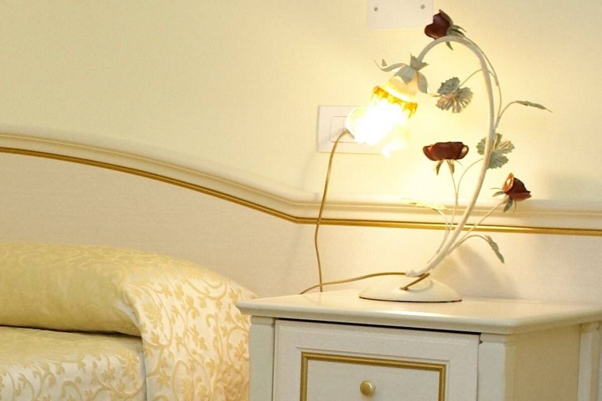 A neatly made bed with a cream-colored bedspread and a matching pillow. There are two bedside tables with lamps, each featuring a floral design.