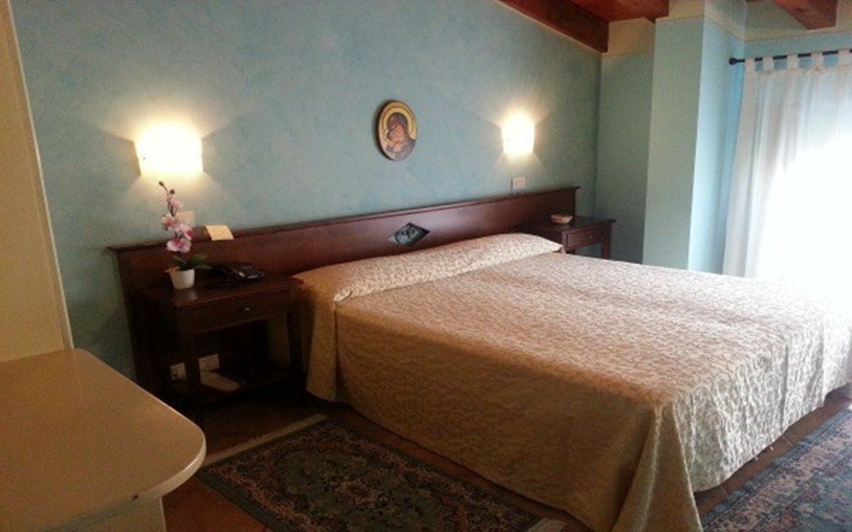 Habitación de hotel con cama, mesitas de noche, lámpara de pared y un pequeño adorno sobre la cama.