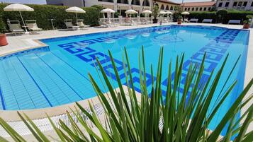 Une grande piscine extérieure dont le fond est recouvert de carreaux décoratifs, entourée de chaises longues et de parasols.