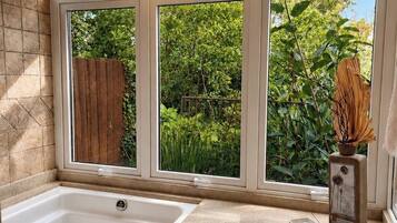 Un baño con bañera, ventana con vista a follaje y cerca de madera.