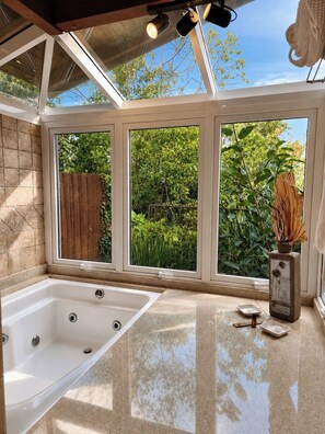 Un baño con bañera, ventana con vista a follaje y cerca de madera.