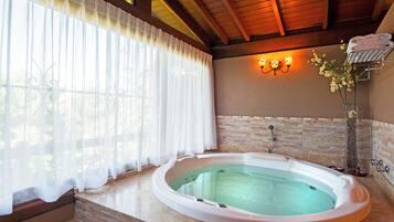 A spa bathroom with a hot tub, stone walls, and a window with sheer curtains.
