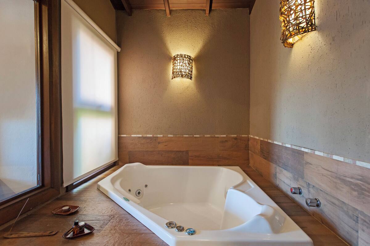 Un baño moderno con una bañera independiente, piso de madera y un accesorio de luz en la pared.
