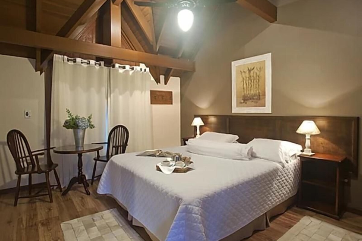A bedroom with a bed, bedside tables, a chair, a small table with a plant, and a painting on the wall.