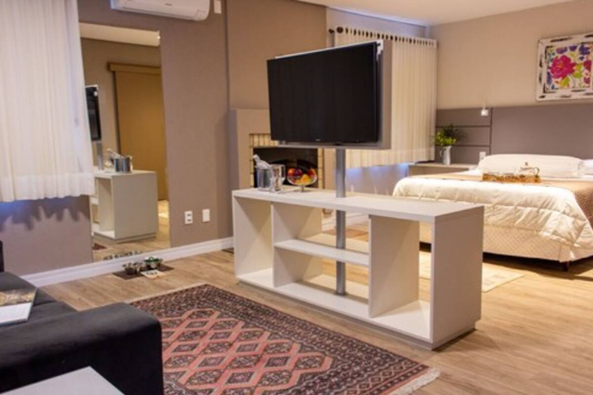Una habitación de hotel moderna con un televisor de pantalla plana sobre una mesa consola blanca, una cama con edredón blanco y una alfombra estampada en el suelo.