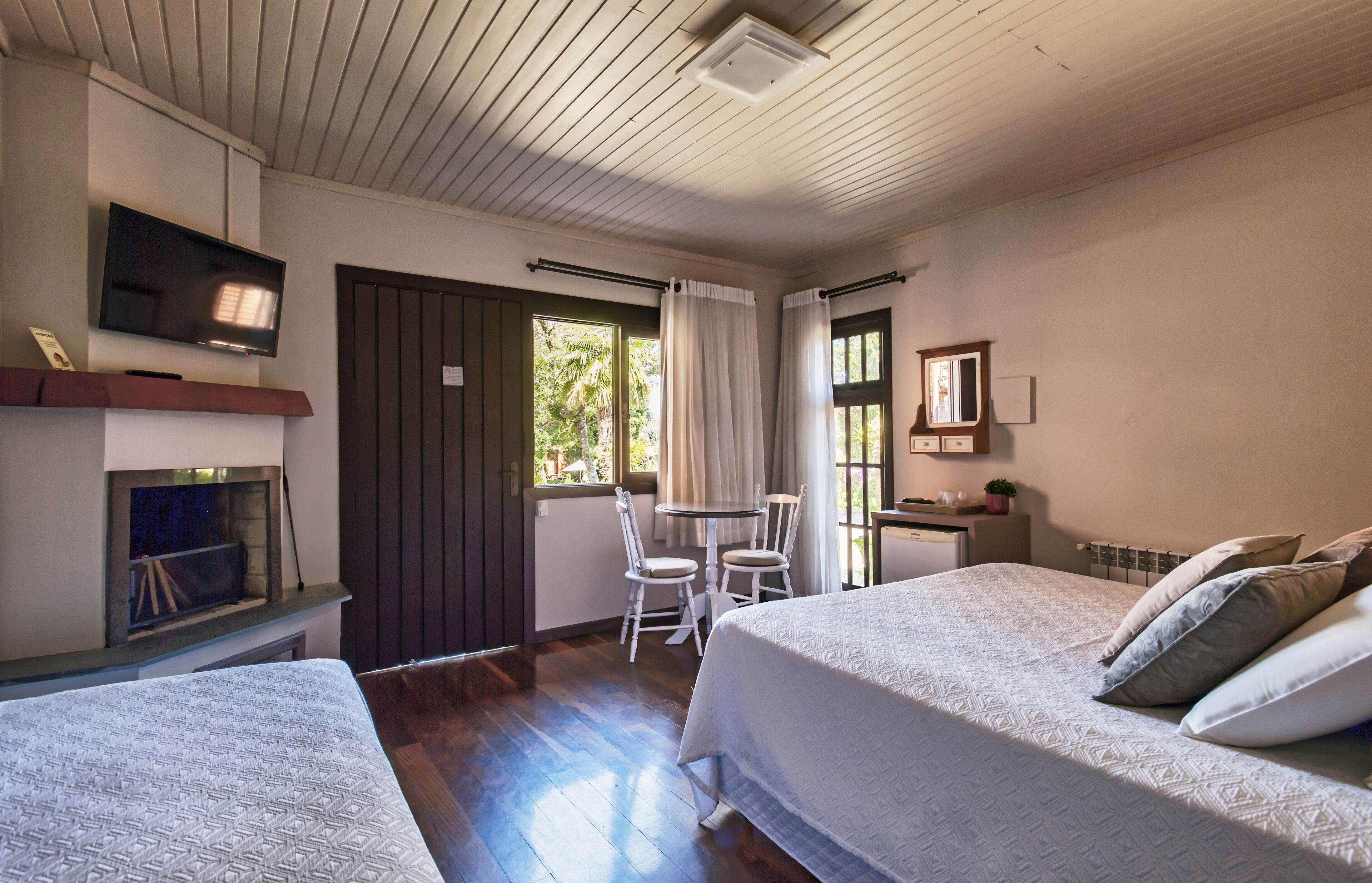 A bedroom with two beds, a TV, a small table with chairs, and a window with curtains.