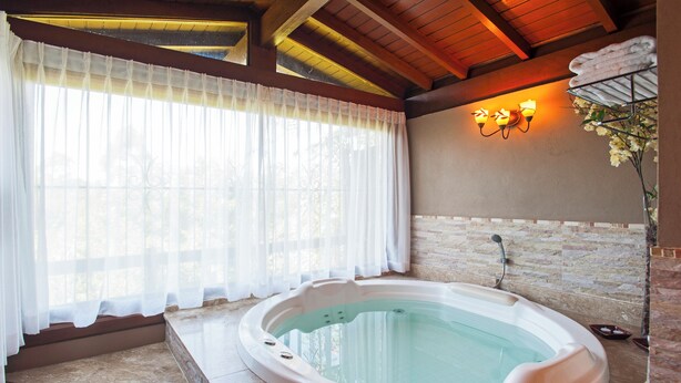 Un'area benessere con vasca idromassaggio, parete in pietra e finestra con tende leggere.